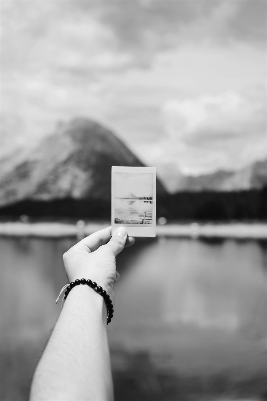 A hand holding up an instant photo in front of a mountain lake